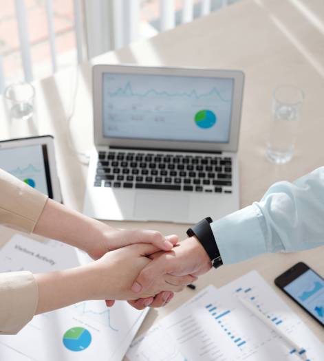 Hands of business people shaking hands over table with various charts and reports after having successful meeting